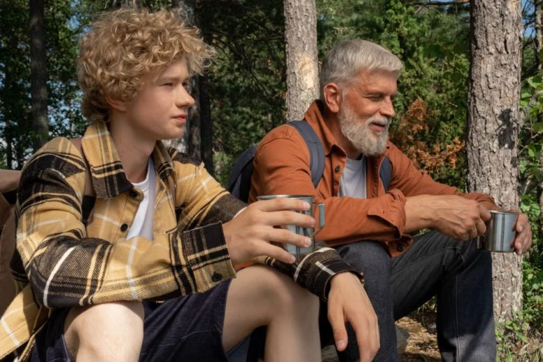 A grandfather and grandson enjoying a break in the forest, sipping from tin cups.